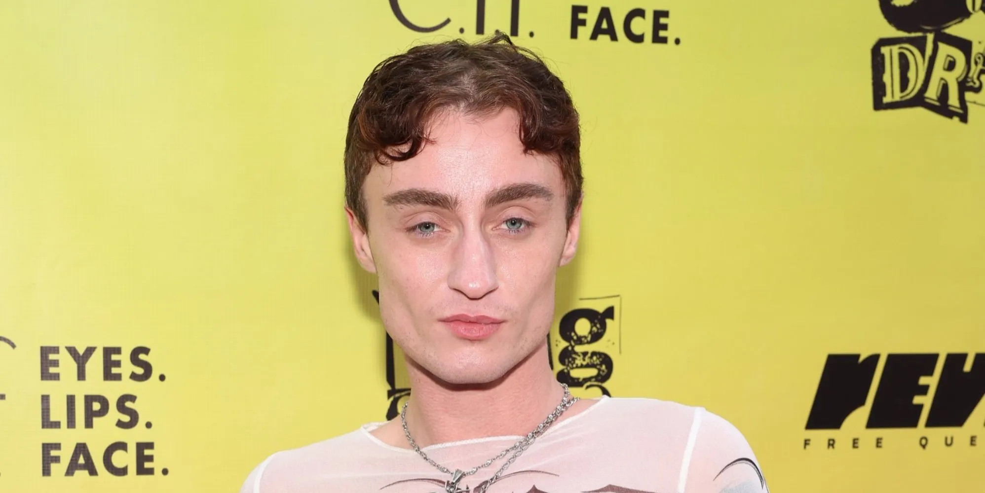 Drag performer Gottmik stands in front of a yellow background at an event.